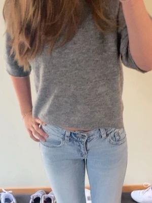 Grå stickad tröja med halvärm - Mysig grå stickad tröja med avslappnad passform och halvärmar. Tröjan har en enkel, stilren design med ribbade kanter vid ärmslut och nederkant. Perfekt till jeans för en chill look. Mycket bra skick och inga defekter!🥰