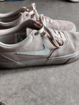 Ljusrosa Nike SB sneakers - Säljer ett par ljusrosa Nike SB sneakers i mocka med vit swoosh på sidan och klassisk svart/vit yttersula. Skorna har snörning och en låg profil som passar perfekt till streetwear. Insidan är vadderad för extra komfort.