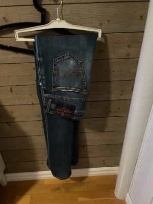 Blå jeans från Jacob Cohën, storlek 31 - Säljer ett par klassiska blå jeans från Jacob Cohën i storlek 31. Jeansen har snygga kontrastsömmar, patch med logga bak och femficksmodell. Tillverkade i mjukt bomullsmaterial med en tvättad finish och orange detaljer vid fickorna.622c 