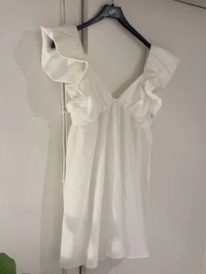 studentklänning från hello molly - Supersöt vit kortklänning med djup v-ringning och stora volangärmar. Den är ifrån hello molly men har tyvärr klippt bort alla lappar i klänningen! Oanvänd endast testad🥰🥰