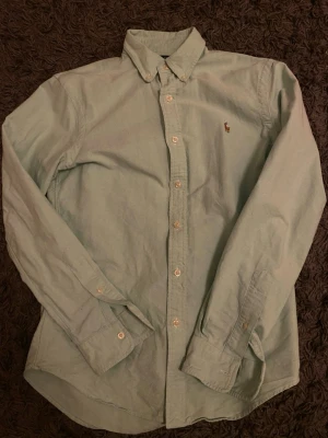 Ljusgrön skjorta från Polo Ralph Lauren - Snygg ljusgrön skjorta från Polo Ralph Lauren i slim fit. Klassisk button-down krage, långa ärmar och vita knappar framtill. Broderad logga på bröstet. Tillverkad i mjuk bomull som känns skön mot huden.