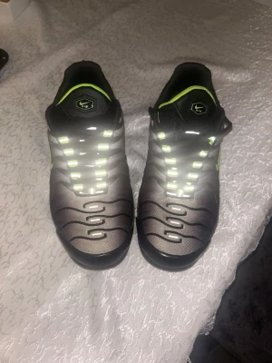 Nike Air Max Plus svart/neongul - Säljer ett par Nike Air Max Plus med svart mesh och syntet, neongula detaljer och reflekterande snören. Skorna har den klassiska Tn Air-loggan bak och synliga Air-enheter i sulan. Perfekta för dig som vill sticka ut med en sportig och modern look.