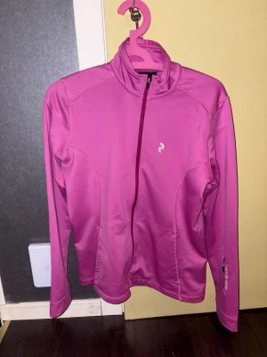 Rosa träningsjacka Peak Performance L - Snygg rosa träningsjacka från Peak Performance i storlek L. Jackan har hel dragkedja framtill, hög krage och är tillverkad i ett mjukt, stretchigt material som passar perfekt till träning eller utomhusaktiviteter. Diskret logga på bröstet och smal passform.