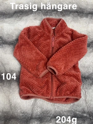Korallfärgad fleecekofta med dragkedja - Mysig korsllfärgad fleecekofta med hög krage och hel dragkedja framtill. Tröjan har ett fluffigt, rutigt strukturmönster och långa ärmar. Perfekt för kyliga dagar och enkel att slänga på sig över en t-shirt.🌸 Sparsamt använd. Hållaren går gått sönder. Storlek 104 