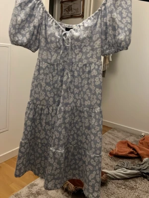 Blommig blå klänning Gina Tricot - Supersöt blå klänning från Gina Tricot med vita blommor, puffärmar och knyt framtill. Klänningen har en luftig passform och är gjord i ett lätt material, perfekt för varma dagar. Den har en midilängd och volangdetaljer som ger en romantisk vibe.