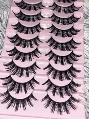 Falska ögonfransar i 9-pack - Säljer ett set med 9 par dramatiska svarta lösögonfransar på rosa bricka. Fransarna är täta och fluffiga med extra volym och längd, perfekta för att skapa en intensiv blick. Materialet är syntetiskt och fransarna har en böjd form för enkel applicering.