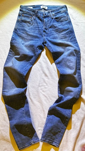 Slim fit jeans Jack & Jones Glenn - Säljer ett par ljusblå slim fit jeans från Jack & Jones, modell Glenn. Klassisk femficksdesign, knappgylf och snygga kontrastsömmar. Jeansen är tillverkade i bomull med en smal passform som sitter snyggt längs benen.