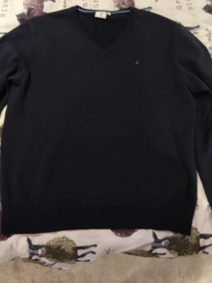 Mörkblå stickad tröja Boomerang - Mörkblå stickad tröja från Boomerang i storlek M. Klassisk v-ringning och diskret broderad logga på bröstet. Tröjan har ribbade muddar vid hals, ärmslut och nederkant. Perfekt för dig som gillar stilrena och tidlösa plagg.