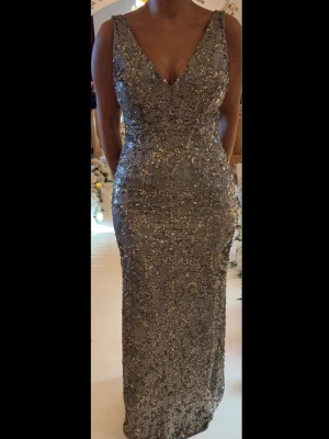 Glittrig långklänning - Säljer en maxad lång confetti-glittrig klänning i silver + guldtoner. Djup v-ringning fram och öppen ry simmarvibe bak. Figurnära passform och skimrande paljetter över hela klänningen. Perfekt för dig som vill sticka ut på bal eller fest.