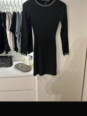 Svart ribbad klänning H&M Divided - Säljer en svart ribbad kortklänning från H&M Divided i storlek 34. Klänningen har lång ärm, rund halsringning med vit randig detalj och samma rand på ärmsluten. Sitter tight och har en sportig vibe.
