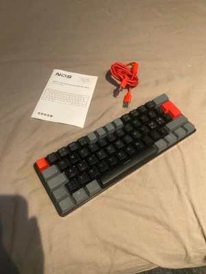 NOS C450 Mini Keyboard Pro RGB - NOS C450 Mini Keyboard Pro RGB med kompakt design, mekaniska tangenter och RGB-belysning. Inkluderar original USB-C kabel och manual. Tangenter och hölje i fint skick utan synligt slitage. Perfekt för gaming eller arbete där platsbesparing är viktigt.