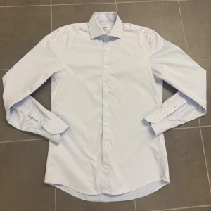 Ljusblå skjorta Stenströms - Säljer en stilren ljusblå skjorta från Stenströms i slimline-modell. Skjortan är tillverkad i twofold super cotton, har klassisk krage, långa ärmar och vita knappar framtill. Perfekt för dig som gillar en clean och klassisk look.