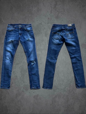 Nudie Jeans Tight Terry blå jeans 31/34 - Säljer ett par blå Nudie Jeans Tight Terry i modellen Sentimental Orange. Jeansen har skinny passform, slitna detaljer på benen och klassiska Nudie-sömmar på bakfickorna. Materialet är 99% ekologisk bomull och 1% elastan för extra stretch.