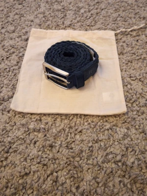 Blå Boggi Milano flätad bälte - Snygg blå flätad bälte från BOGGI MILANO i storlek 85, ca 108 cm lång. Använd fåtal gånger och skicket är i princip som ny, inga slitningar eller defekter finns. Passar jättebra som en stilig och lyxig accessoar till vardagen. Dustbag ingår. Skick: 9/10