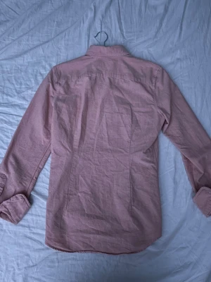 Rosa skjorta från Ralph Lauren - Snygg rosa skjorta från Ralph Lauren med klassisk button-down krage och broderad logga på bröstet. Skjortan har långa ärmar och vita knappar framtill. Tillverkad i mjuk bomull som är skön mot huden och har en normal passform.