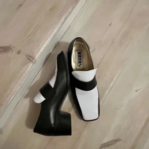 Svartvita loafers från Bronx - Unika loafers från Bronx i svart och vitt skinn med fyrkantig tå och bred klack. Stilen ger en cool retrovibe. Perfekt för dig som gillar att sticka ut med en kombination av lite edge och klassisk form. Superskön passform, har använts med tunn innersula av modellen som har strl 38. (Nypris 699kr Scorett)