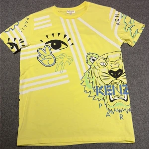 Gul Kenzo t-shirt med grafiskt tryck - Kenzo t-shirt i stark gul färg med coola grafiska tryck som tiger, öga, palmer, smiley och peace-tecken. T-shirten har rund hals, korta ärmar och är tillverkad i mjuk bomull. Perfekt för dig som gillar statement-plagg och streetstyle.