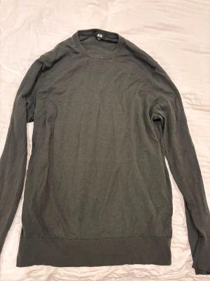 Mörkgrön stickad tröja från Uniqlo - Snygg mörkgrön stickad tröja från Uniqlo i storlek XL. Tröjan är tillverkad i 100% ull och har en klassisk rund halsringning samt långa ärmar. Perfekt för dig som gillar enkel och stilren design med mjukt material.