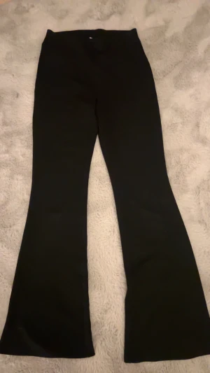 Svarta bootcut byxor - Snygga svarta bootcut byxor med klassisk siluett och utsvängda ben. Perfekta för dig som gillar en stilren look med lite edge. Byxorna har en enkel design utan synliga detaljer och passar till många olika outfits.