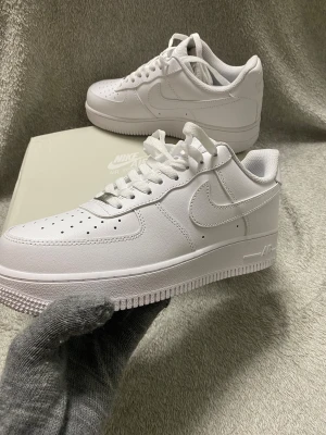 Helt nya Nike Air Force 1  helvita sneakers - Nike Air Force 1 Low i helvitt med klassisk design, perforerad tå och snörning. Snyggt skinnmaterial och platt sula ger en clean och fräsch look. Ikonisk Swoosh på sidan och Air-detalj på sulan. Perfekt för dig som gillar stilrena sneakers. Äkta🤩          Skickas samma dag eller nästa dag 🤩☺️    Säljer även billigt för att det är snart julafton och folk behöver köpa presenter 
