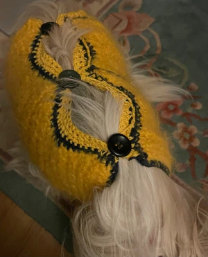 Gul stickad kofta med svarta knappar - Säljer en handstickad gul kofta med svarta detaljer och stora svarta knappar. Koftan har en grovstickad struktur och är designad för mindre hundar. Svarta kanter ger en snygg kontrast och knapparna gör den enkel att ta av och på. Perfekt för att ge din hund extra stil och värme.