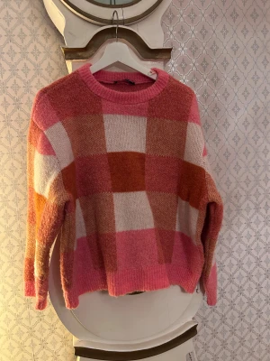 Rutig rosa tröja från Gina Tricot - Säljer en mysig rutig tröja från Gina Tricot i storlek M. Tröjan har breda rutor i rosa, orange och beige toner, rund hals och långärmad passform. Materialet är mjukt och fluffigt, tillverkat av 70% akryl och 30% polyamid. Perfekt för dig som gillar färg och mönster!
