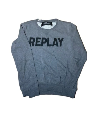 Grå sweatshirt från Replay - Snygg grå sweatshirt från Replay med stort svart tryck över bröstet. Tröjan har rund hals, långa ärmar och ribbade muddar vid ärmslut och nederkant. Perfekt för dig som gillar enkel och stilren streetwear.
