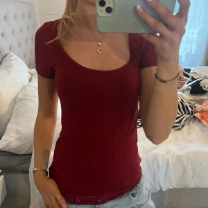 Vinröd topp med spets från Zalando - Säljer en vinröd topp från Zalando Essentials i storlek S. Toppen har rundad halsringning, korta ärmar och en snygg spetskant längst ner. Materialet är mjukt och stretchigt, perfekt för dig som gillar en slim passform och vill ha en enkel men ändå detaljrik look.