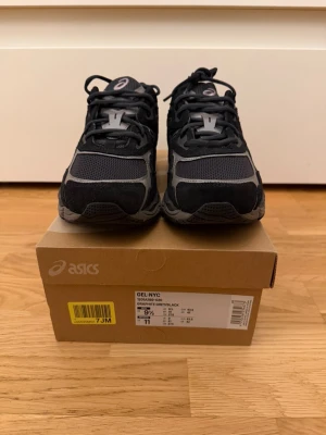 ASICS GEL-NYC graphite grey sneakers - ASICS GEL-NYC sneakers i graphite grey och svart med mesh och mockadetaljer. Snyggt sportig design med snörning och platt sula. Ikoniska ASICS-stripes på sidan och dämpad yttersula för extra komfort. Perfekt för dig som gillar streetwear och sportig stil.