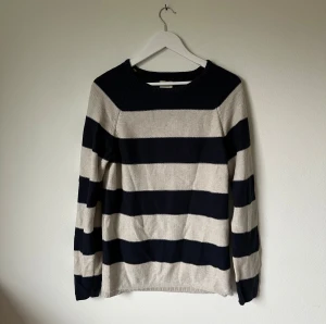 Randig bomullströja från Selected Homme - Snygg långärmad tröja från Selected Homme i storlek L. Tröjan är stickad i 100% bomull och har breda marinblå och beige ränder. Rund halsringning med ribbad kant och klassisk passform. Perfekt för dig som gillar enkel och stilren design. 4Ö9