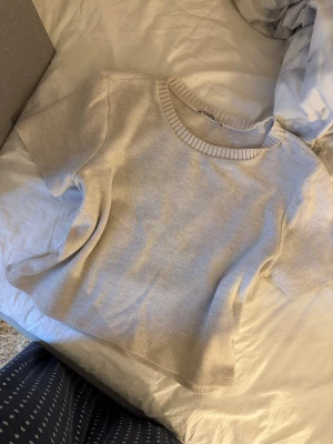 Beige stickad topp med kort ärm - Säljer en ljusbeige stickad topp med rund hals och korta ärmar. Toppen har en ribbad kant vid halsen och är i mjukt material som känns skönt mot huden. Perfekt att styla med jeans eller kjol för en chill look.