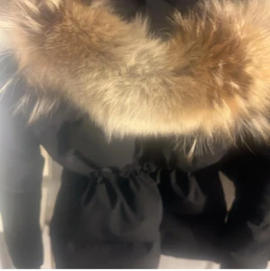 Svart vinterjacka  med päls från Canada Goose - Säljer en svart vinterjacka från Canada Goose Chelsea Parka Heritage, med fluffig päls runt huvan. Jackan har en snygg, quiltad design, dragkedja framtill och klassisk logga på ärmen. Perfekt för kalla dagar och har en riktigt schysst look som sticker ut.