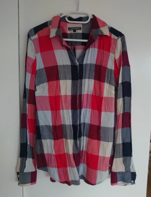 Rutig skjorta från Tommy Hilfiger, stl 38, dam - Snygg rutig skjorta från Tommy Hilfiger i bomull med stora rutor i rött, vitt, grått och marinblått. Klassisk krage, långa ärmar med knappar vid manschetten och Hilfiger-detalj på sidan. Perfekt för dig som gillar en chill och färgstark stil.