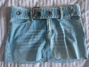 Blå jeanskjol från Crocker med bälte - Snygg ljusblå jeanskjol från Crocker i storlek S. Kjolen har rå kant nertill, klassiska fickor fram och bak samt ett brett jeansbälte med stora metallöljetter, bältet går att ta av. Perfekt för dig som gillar en chill och trendig denimlook.
