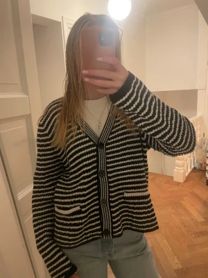 Svartvit randig kofta med knappar - Säljer en svartvit randig kofta med v-ringad hals och tre stora knappar framtill. Koftan har två små fickor och är stickad i mjukt material. Passar perfekt till jeans och har en loose fit som ger en chill vibe.