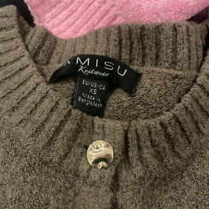 Brun stickad väst i strl XS - Mysig brun stickad väst med ribbade kanter och sex silvriga knappar framtill. Perfekt att styla över en skjorta eller t-shirt för en chill look. Materialet är mjukt och ger en skön känsla, och den neutrala färgen gör den enkel att matcha.