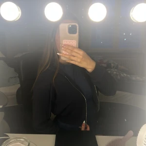 Mörkblå hoodie med dragkedja cropped - Snygg mörkblå hoodie med huva och hel dragkedja framtill. Tröjan har långa ärmar och ribbade muddar vid ärmslut och nederkant. Perfekt för chill dagar och enkel att matcha med jeans eller leggings.