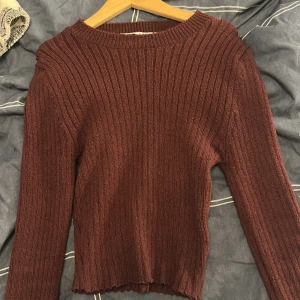 Vinröd ribbad stickad tröja Zara - Säljer en vinröd stickad tröja från Zara i storlek M. Tröjan har ett ribbat mönster, rund halsringning och långa ärmar. Materialet är mjukt och stretchigt, perfekt för att hålla dig varm under kyliga dagar. Snygg att styla med jeans eller kjol.
