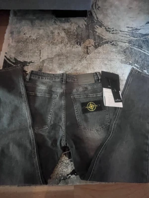 stone island jeans - Säljer ett par grå jeans från Stone Island med klassisk bakficka och den ikoniska kompasspatchen. Jeansen har en rak passform och är tillverkade i slitstarkt bomullsmaterial. Perfekt för dig som gillar streetwear och vill ha en snygg detalj i outfiten.