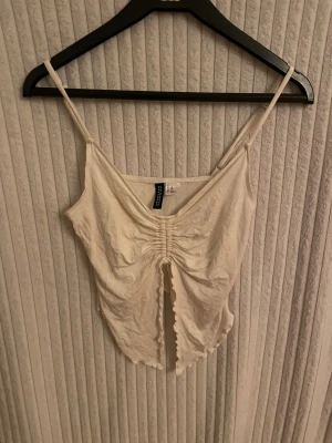 Vit linnetopp med snörning - Säljer en ljusvit linnetopp med smala axelband och snygg snörning framtill. Toppen har en v-ringad design och croppad passform med vågig kant nedtill. Den är i bra skick och säljs i befintligt skick.