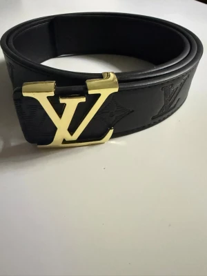 Louis vuitton bälte - Säljer ett riktigt snyggt Louis Vuitton-bälte i svart skinn med klassiskt LV-monogram i guld. Har ett svart spänne och en präglad logga på insidan. Vid minsta fundering – tveka inte på att höra av er!