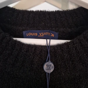 Svart stickad tröja Louis Vuitton - Svart stickad tröja från Louis Vuitton med stort vitt LV-logo på bröstet. Klassisk rund halsringning och långa ärmar. Perfekt för dig som vill ha en stilren men ändå lyxig look. Passar även en storlek S.