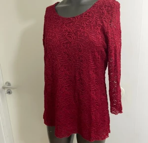 Röd spetsblus med lång ärm - Säljer en snygg röd blus i spets med lång ärm och rund hals. Blusen har ett detaljerat spetsmönster och är fodrad med ett mjukt tyg under. Perfekt för dig som gillar att sticka ut med färg och coola detaljer.