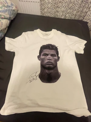 Vit t-shirt med tryck och autograf - Vit t-shirt med korta ärmar och ett stort svartvitt tryck av en person på framsidan. Trycket har en cool autograf under motivet. Klassisk rund hals och rak passform, perfekt för dig som gillar statement-plagg.