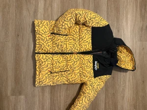 Gul och svart pufferjacka från Panda - Säljer en fet pufferjacka från Panda med gul och svart färg, coolt abstrakt mönster och huva. Jackan har dragkedja framtill och fickor med dragkedja. Perfekt för dig som vill sticka ut med en unik stil och hålla dig varm.