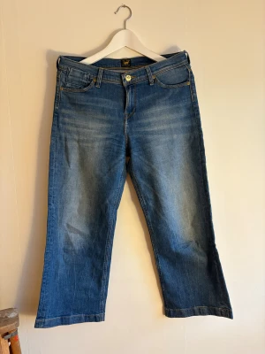 Blå Lee jeans med raka ben - Snygga blå jeans från Lee med klassisk femficksdesign och raka ben. Modellen är lite kortare, typ 3/4 byxa och är tillverkade av 99% bomull och 1% elastan för lite stretch. De har gul kontrastsöm och Lee-logga på bakfickan och linningen.