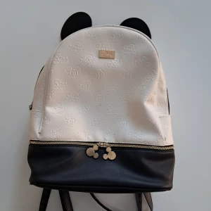 Disney ryggsäck med Mickey Mouse-detaljer - Supersöt ryggsäck från Disney i vitt och svart med präglade Mickey Mouse-motiv över hela väskan. Väskan har svarta öron upptill, guldfärgade kedjedetaljer och dragkedjor med Mickey-berlocker. Tillverkad i syntetmaterial och perfekt för dig som älskar Disney.