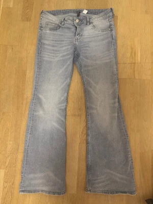 Bootcut ljusblå jeans från Divided - Snygga ljusblå bootcut jeans från Divided i storlek 42. Klassisk femficksmodell med normal passform och låg midja. Jeansen har en lätt tvättad look och är tillverkade i mjukt denimtyg. Perfekt för dig som gillar retrovibbar och avslappnad stil. Aldrig använda