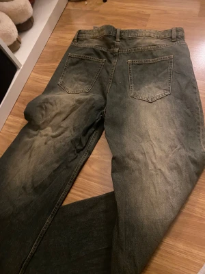 Wide jeans från Bershka i mörk tvätt - Säljer ett par mörkgrå jeans från Bershka med breda ben och klassisk femficksdesign. Jeansen har en cool tvätt med slitningar och kontraster, samt normal passform i midjan. Perfekt för dig som gillar en avslappnad och trendig look.