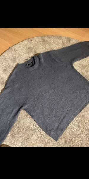 Mörkblå stickad tröja med rund hals - En enkel och snygg mörkgrå stickad tröja från H&M med rund hals och långa ärmar. Perfekt för dig som gillar en clean look och vill ha något mjukt och bekvämt. Tröjan har ribbade muddar vid ärmslut och nederkant.